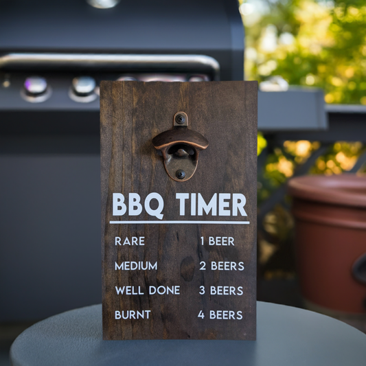 A wooden bottle opener with the text 'BBQ TIMER' and a list of instructions for grilling, placed on a table next to a BBQ grill. Fum, quirky gift for men