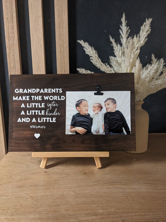 A wooden photo plaque with a black text overlay reading 'GRANDPARENTS MAKE THE WORLD A LITTLE SOFTER, A LITTLE KINDER, AND A LITTLE WARMER.' attach your favourite photo to the bulldog clip